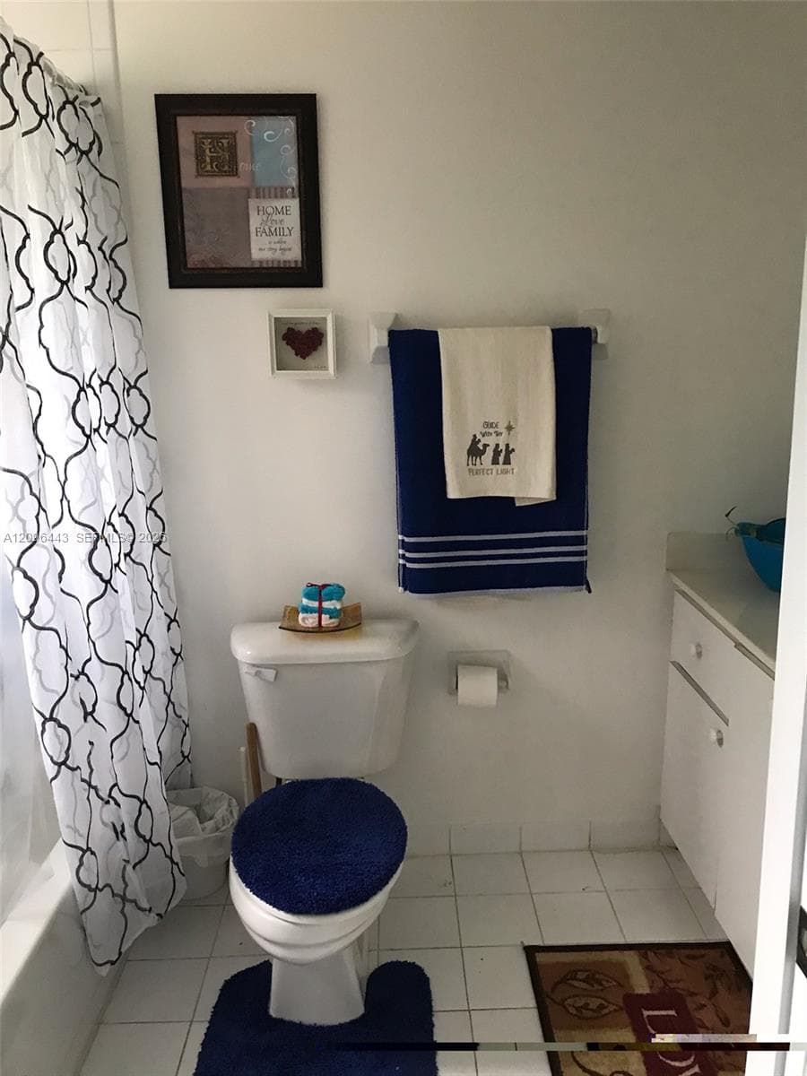 Full bathroom featuring white ceramic floor tiling, a white vanity cabinet with a stone countertop, a standard toilet, and a combination bathtub and shower enclosure