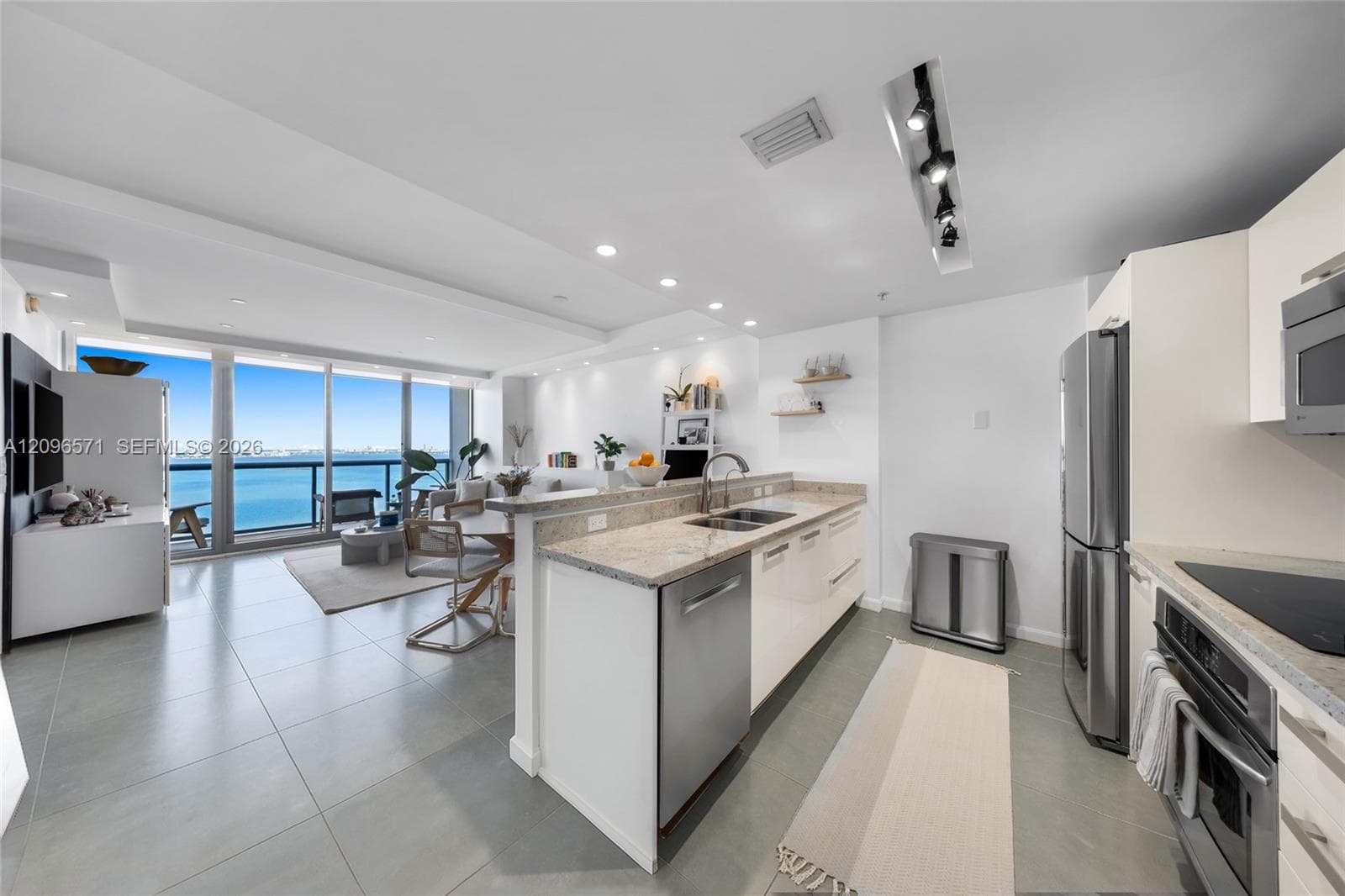 Kitchen featuring high-gloss cabinetry, stone countertops, stainless steel appliances, recessed ceiling lighting, and large-format tile flooring