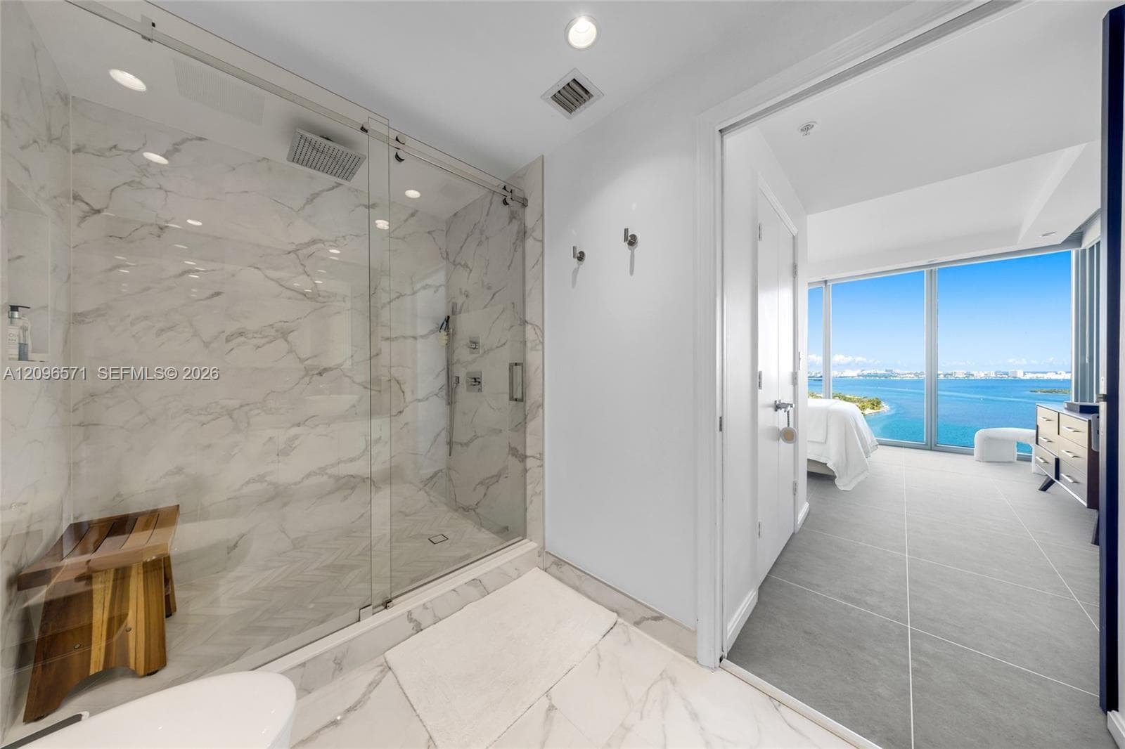 Walk-in shower with floor-to-ceiling veined tile, frameless glass enclosure, rain-style showerhead, and integrated wall niche