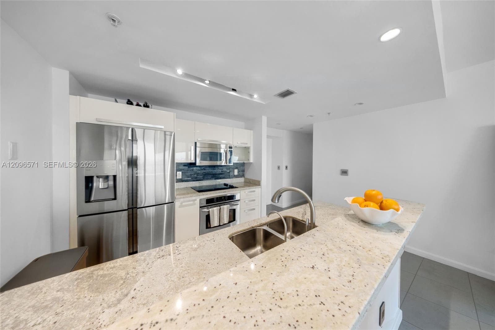 Kitchen featuring glossy flat-panel cabinetry, stone-finish countertops, stainless steel appliances, a deep double-basin undermount sink with a gooseneck faucet, and a decorative tile backsplash