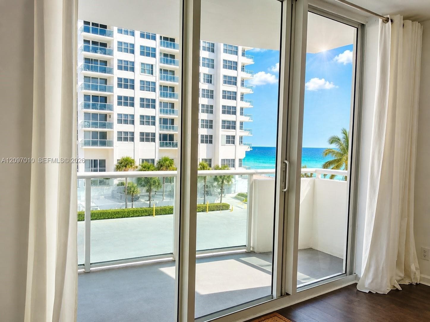 Floor-to-ceiling glass sliding doors opening to a private balcony with glass railings and ocean horizon scenery