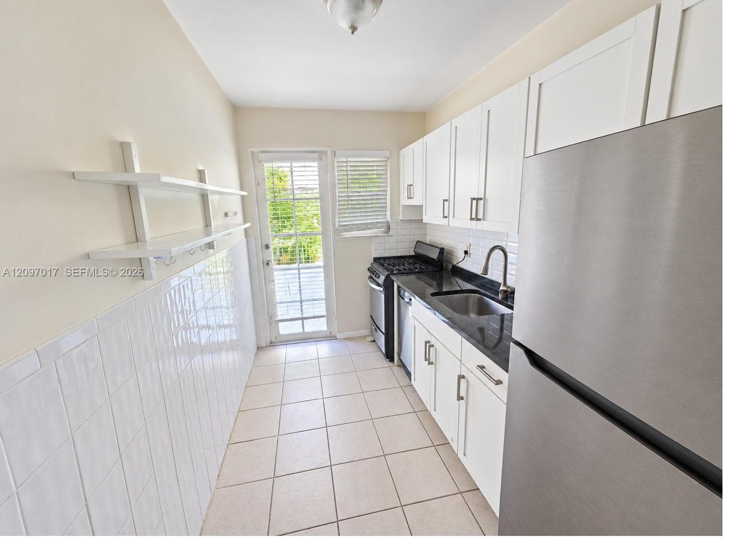 Kitchen featuring white cabinetry, dark stone countertops, tile wall backsplash, stainless steel appliances, and ceramic tile flooring