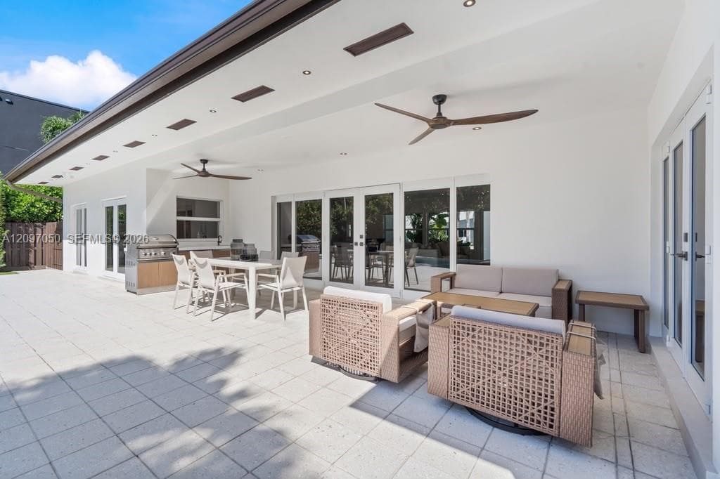 Covered outdoor patio featuring large-format tile flooring, built-in outdoor kitchen, ceiling-mounted fans, recessed lighting, and glass-paneled double doors