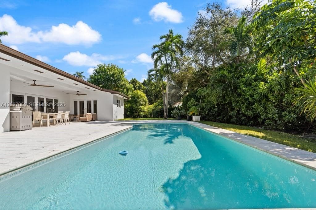 Rectangular in-ground swimming pool with a paved patio, covered terrace, integrated ceiling fans, and mature perimeter landscaping