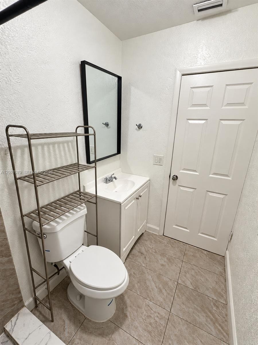 Bathroom featuring a vanity cabinet with an integrated sink, polished chrome faucet, rectangular wall-mounted mirror with a black frame, and neutral-toned tile flooring