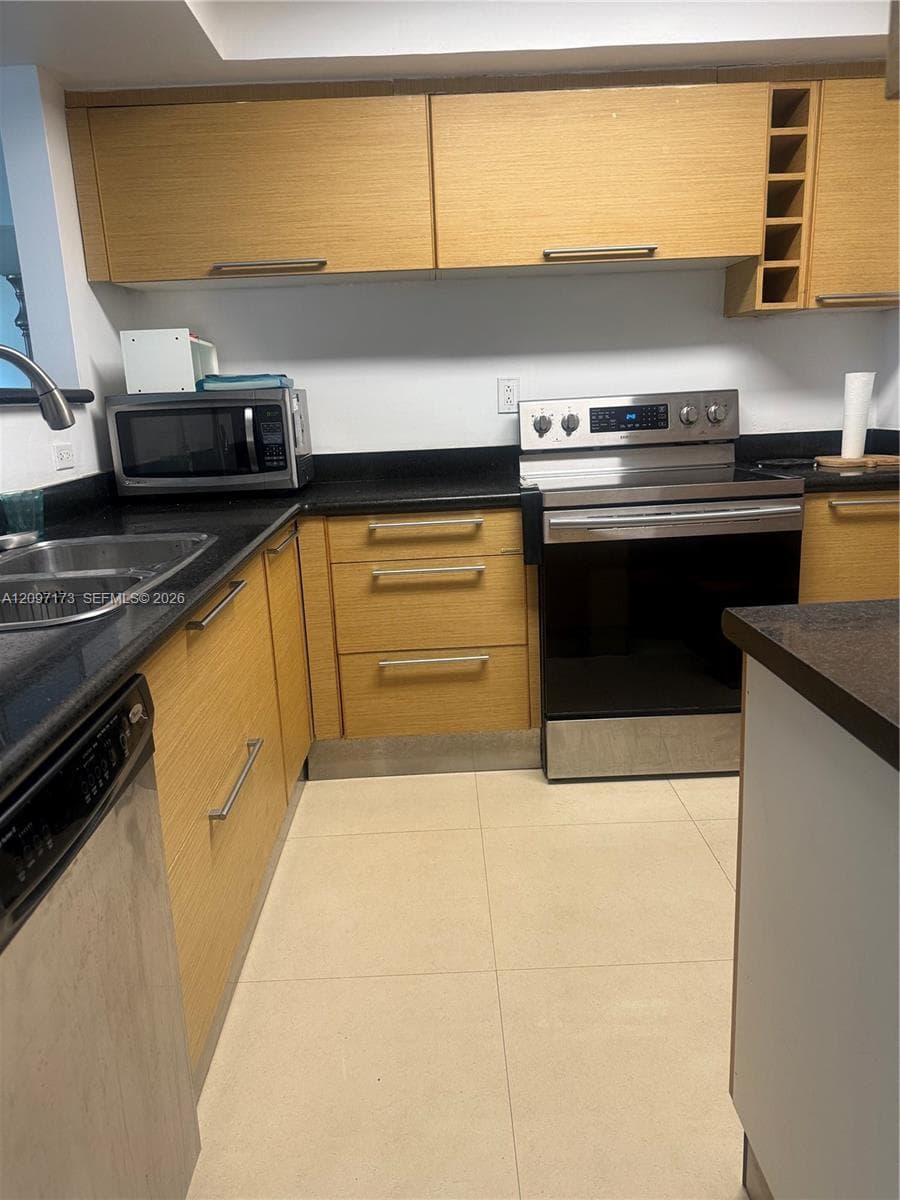 Kitchen featuring flat-panel wood-finish cabinetry, built-in wine storage, dark solid-surface countertops, stainless steel appliances, and tile flooring