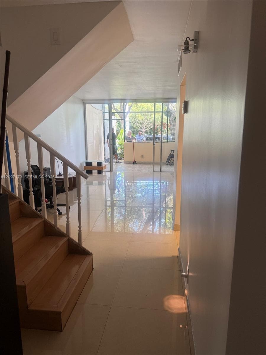 Interior space featuring polished stone flooring, staircase with wood treads, painted wood balustrades, and expansive floor-to-ceiling glass sliding doors