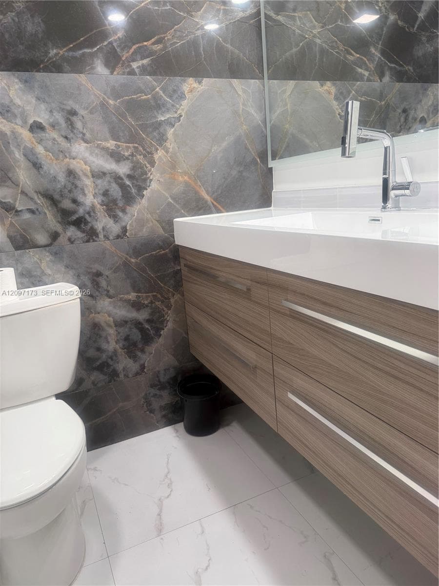 Floating wood-finish vanity with a white rectangular sink, polished chrome faucet, large-format dark stone-patterned wall tile, and light stone-patterned floor tile