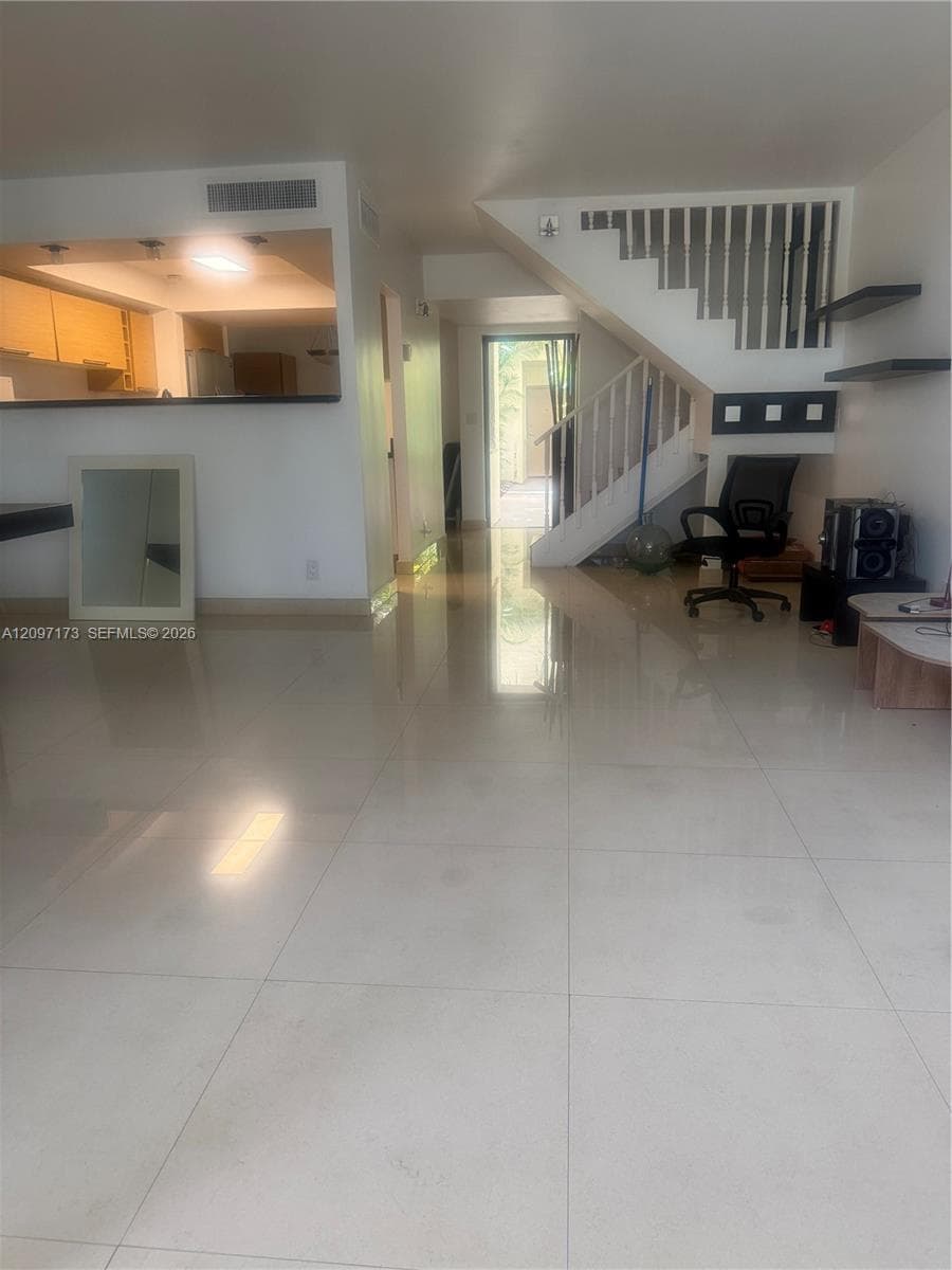 Large format tile flooring, built-in shelving, staircase with metal railing, and kitchen pass-through counter