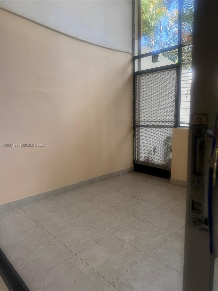 High-ceilinged room featuring neutral wall tones, large-format tile flooring, and a floor-to-ceiling metal-framed screen door