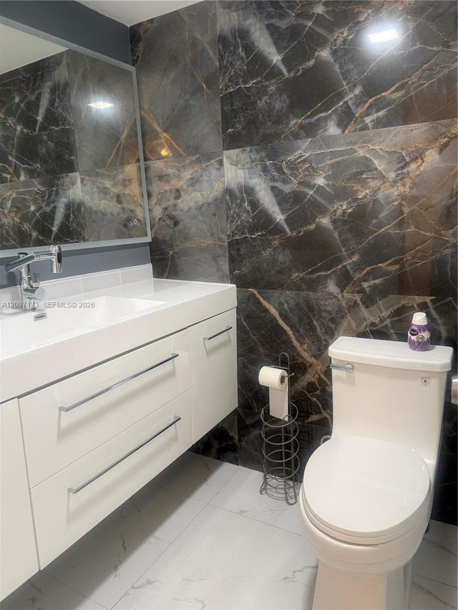 Floating vanity with white cabinetry, integrated sink, polished chrome faucet, and large-format high-contrast decorative wall tile