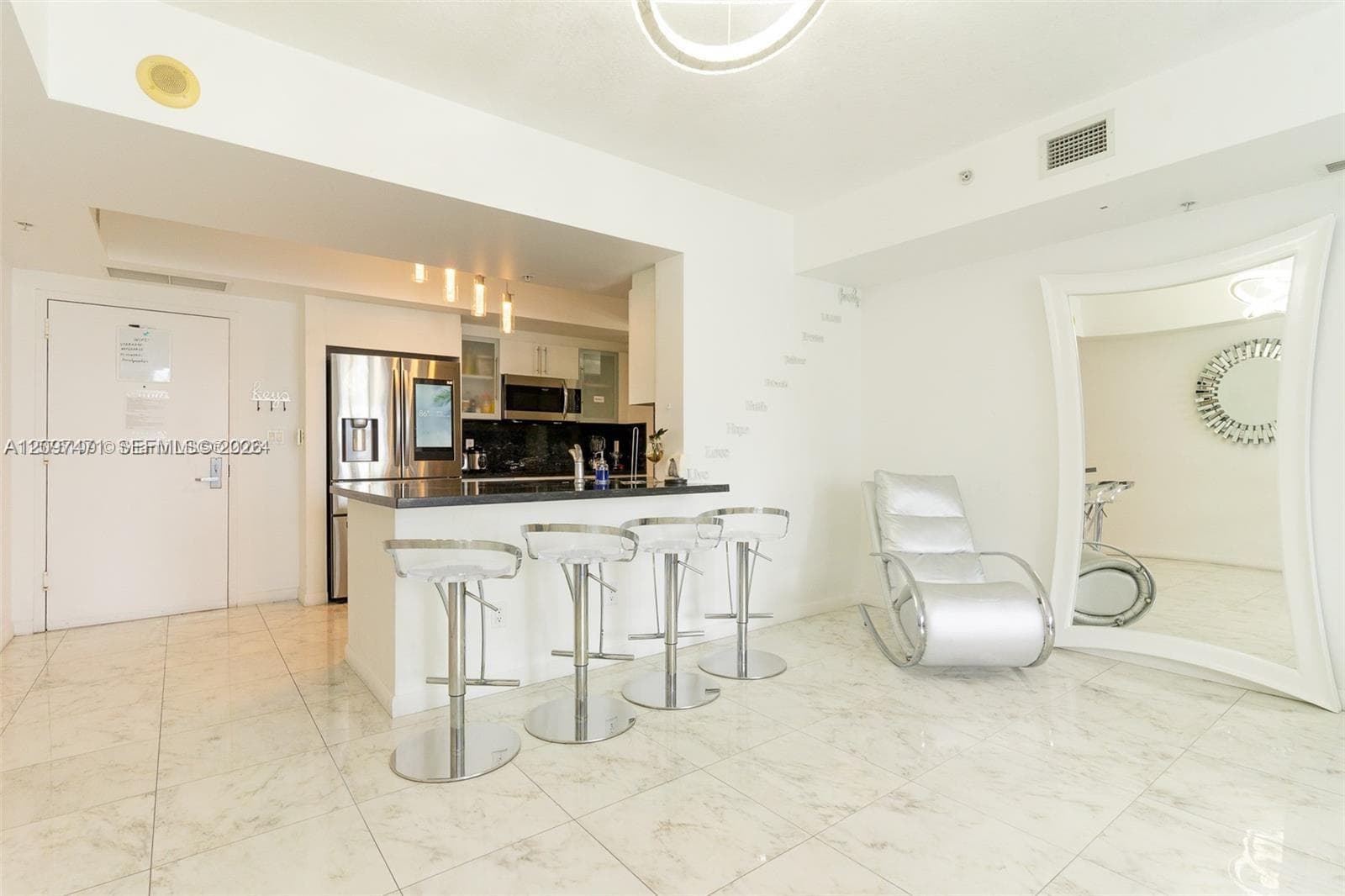 Kitchen area featuring a stone-topped breakfast bar, stainless steel refrigerator, dark cabinetry, recessed lighting, and polished stone-finish flooring