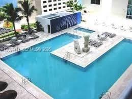 Outdoor swimming pool featuring a central paved island, built-in steps, surrounding stone-finish deck, and palm trees
