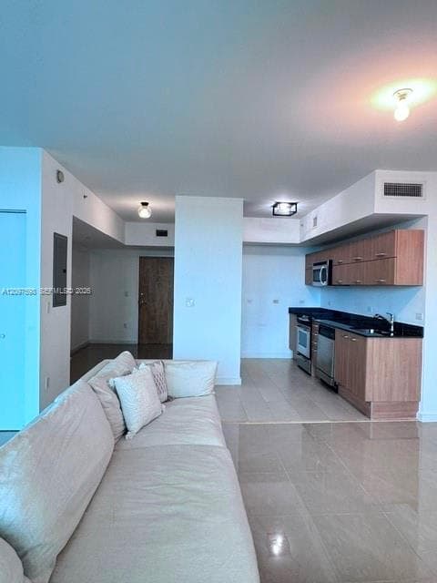 Kitchen featuring wood-finish cabinetry, dark stone countertops, stainless steel appliances, and large-format tile flooring