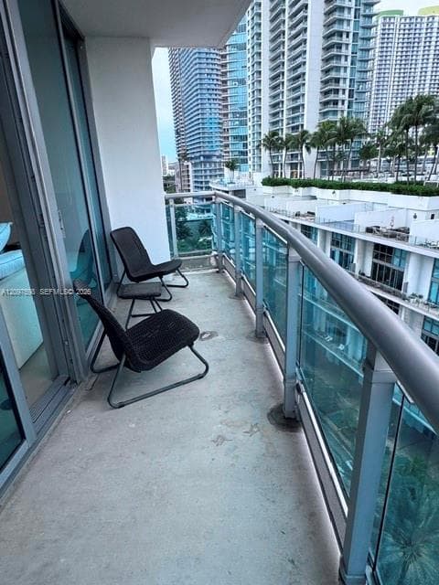 Private balcony featuring a concrete floor, floor-to-ceiling glass sliding doors, and a metal railing with glass panels