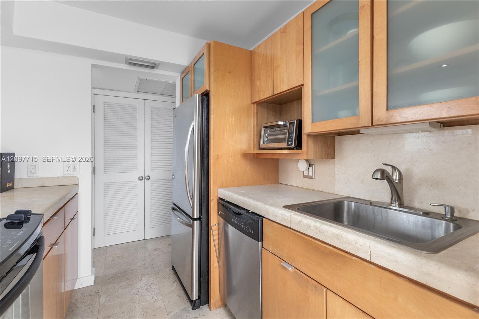 Kitchen featuring light wood cabinetry, stainless steel appliances, stone countertops, and a full-height stone backsplash