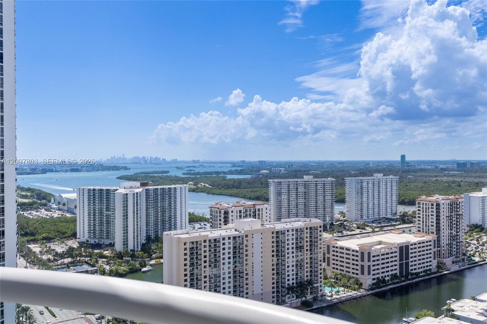 Elevated balcony featuring a cylindrical metal railing overlooking an expansive coastal landscape, deep-water canals, and regional metropolitan skyline