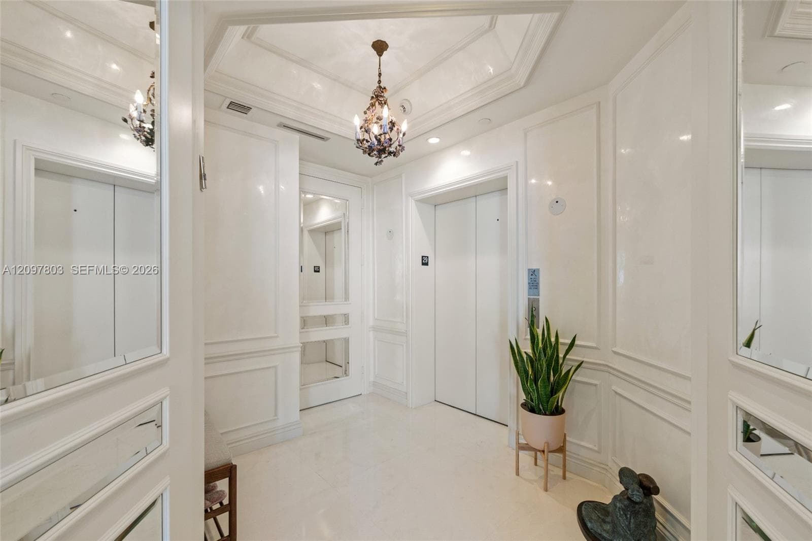 Grand foyer featuring white wainscoting, an octagonal tray ceiling, a polished chandelier, and stone flooring