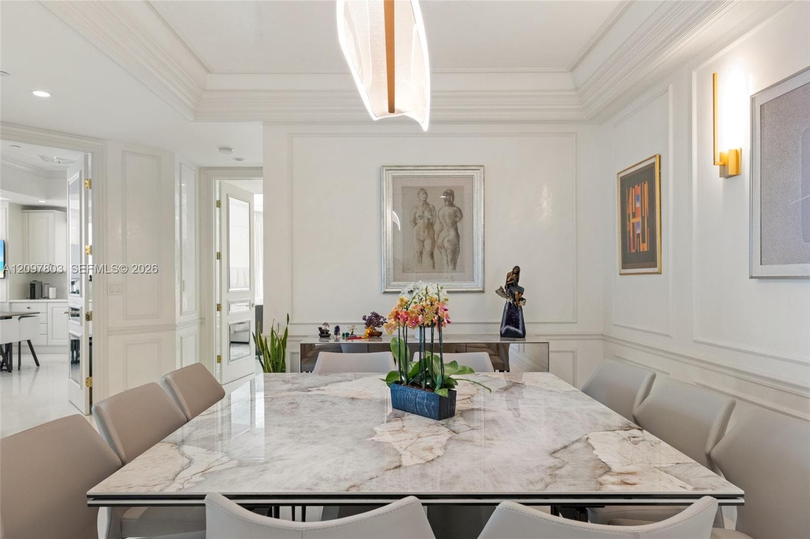 Dining area featuring recessed ceiling details, white wall molding, contemporary pendant lighting, wall-mounted sconces, and polished stone-finish flooring