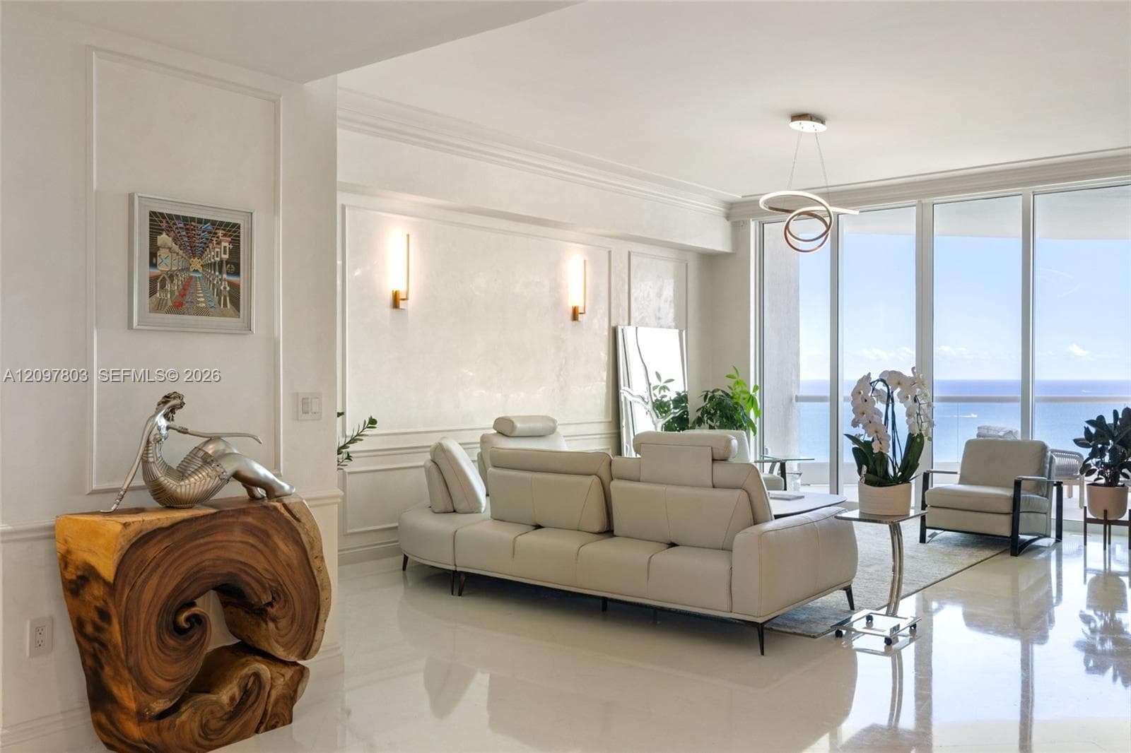 Floor-to-ceiling glass windows, custom wall paneling, polished stone flooring, contemporary multi-ring pendant lighting, and wall-mounted sconces