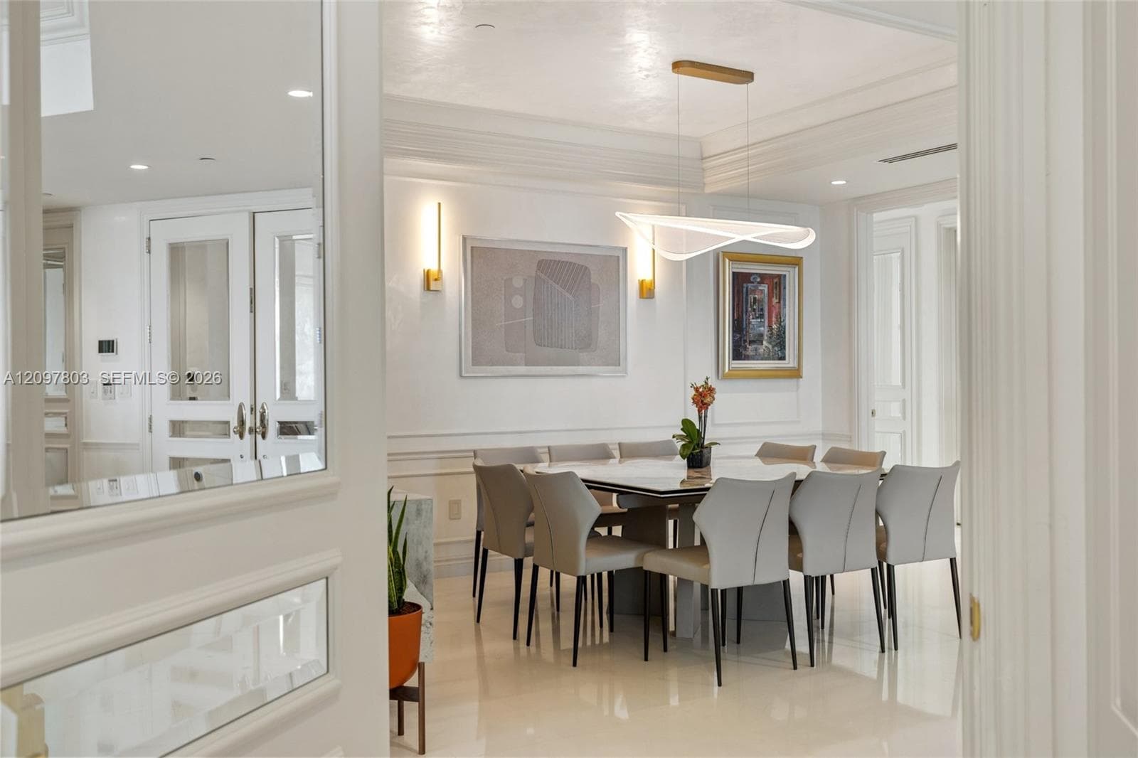 Dining area featuring crown molding, wainscoting, polished stone flooring, custom wall-mounted sconces, and a sculptural modern chandelier