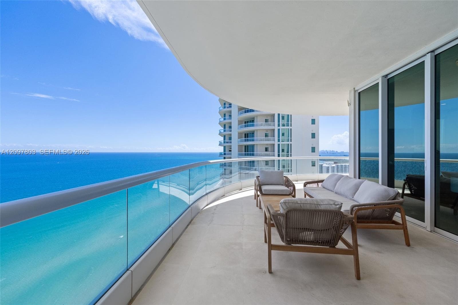 Expansive curved balcony featuring light-toned flooring, glass panel railings, and full-height sliding glass doors