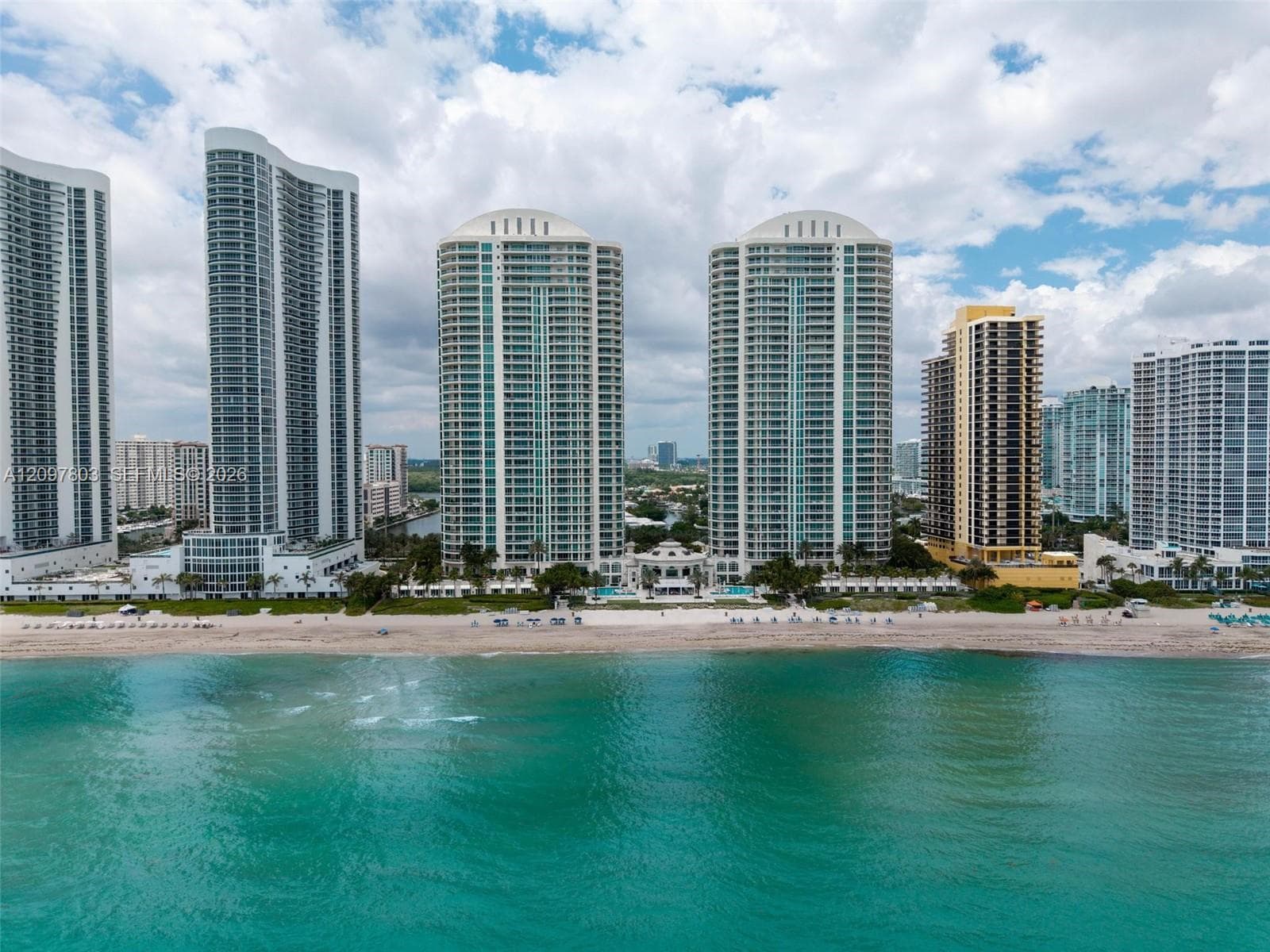 High-rise coastal towers featuring direct beach access, glass-paneled balconies, arched architectural detailing, and outdoor swimming pools