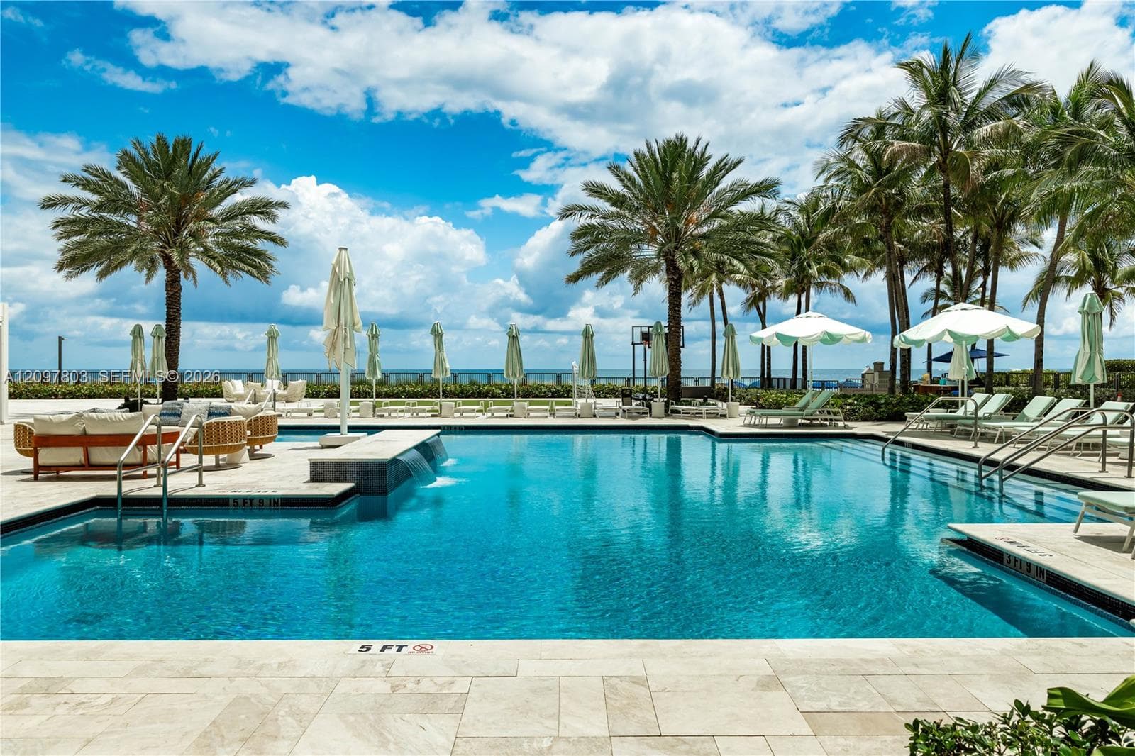 Swimming pool with a water feature, stone paver decking, and perimeter palm trees