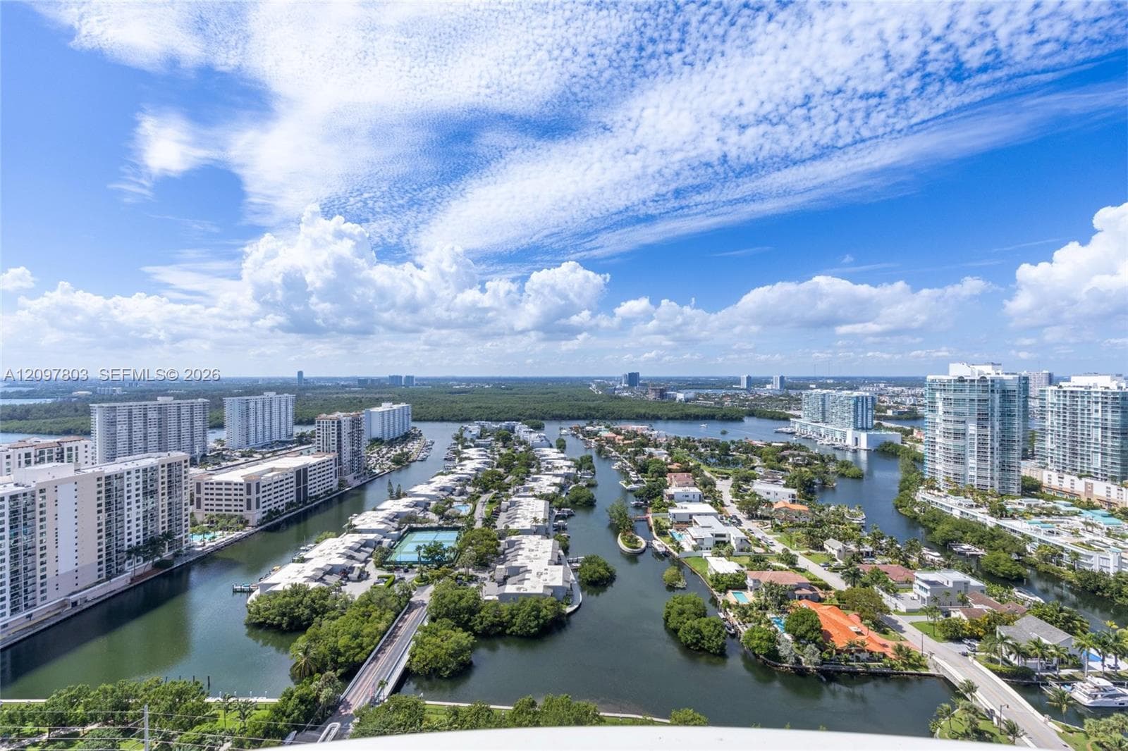 High-rise aerial perspective featuring expansive water frontage, deep-water canal access, mature coastal vegetation, and multi-story residential architecture