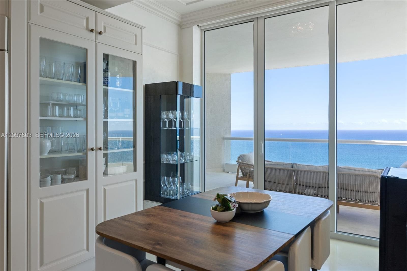 Built-in floor-to-ceiling cabinetry with glass-panel doors, floor-to-ceiling glass wall, and balcony access featuring an ocean backdrop