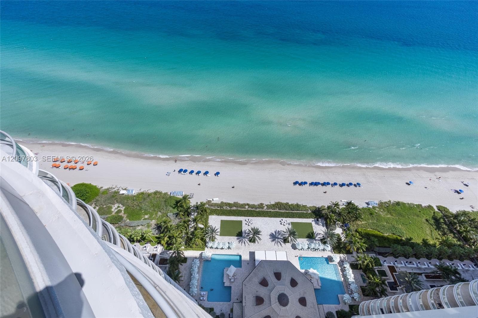 Elevated perspective featuring curved balcony architecture, expansive ocean frontage, dual swimming pools, and manicured terrace landscaping