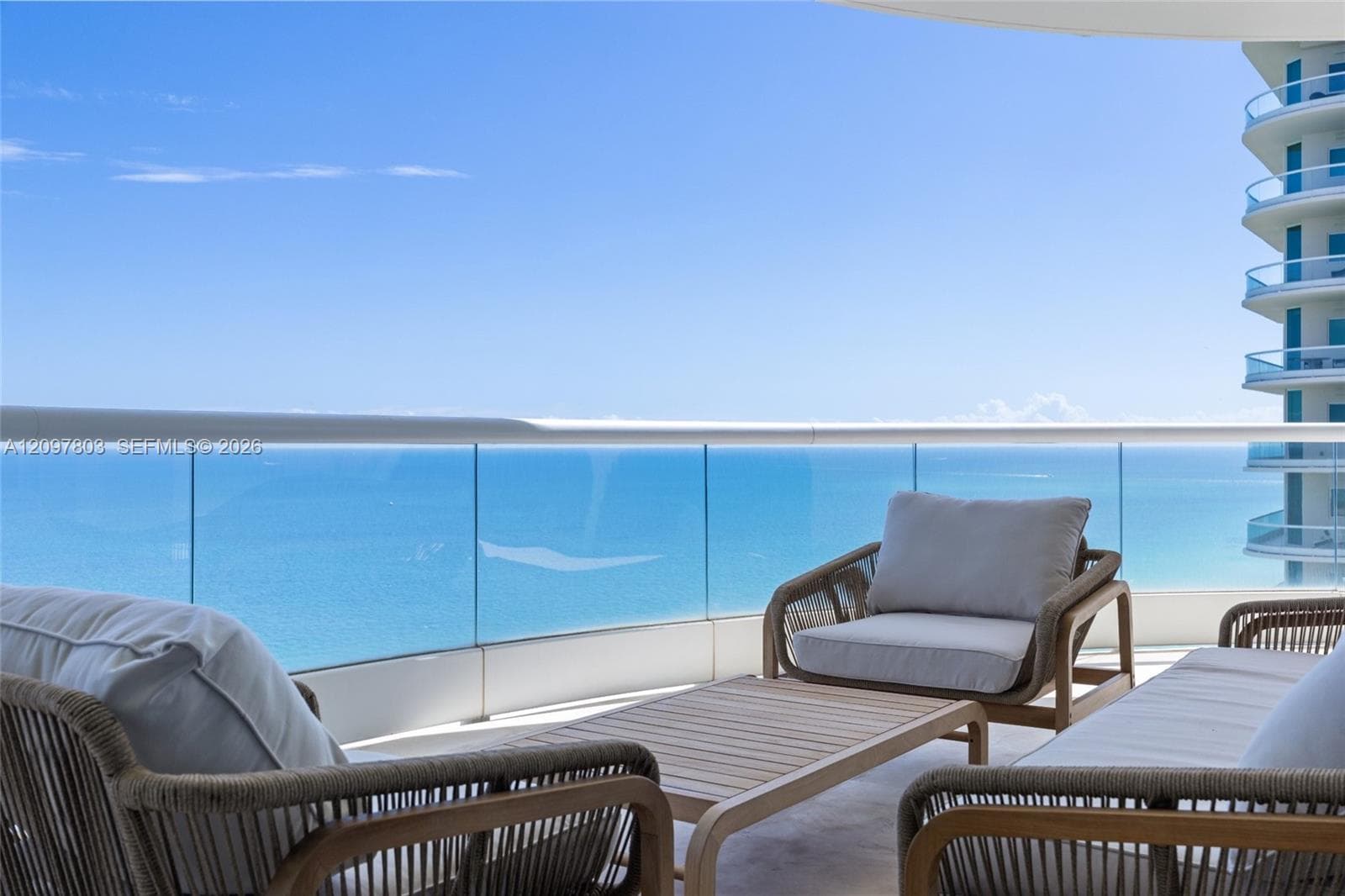 Expansive balcony featuring a glass panel railing, stone flooring, and an open-air ocean horizon