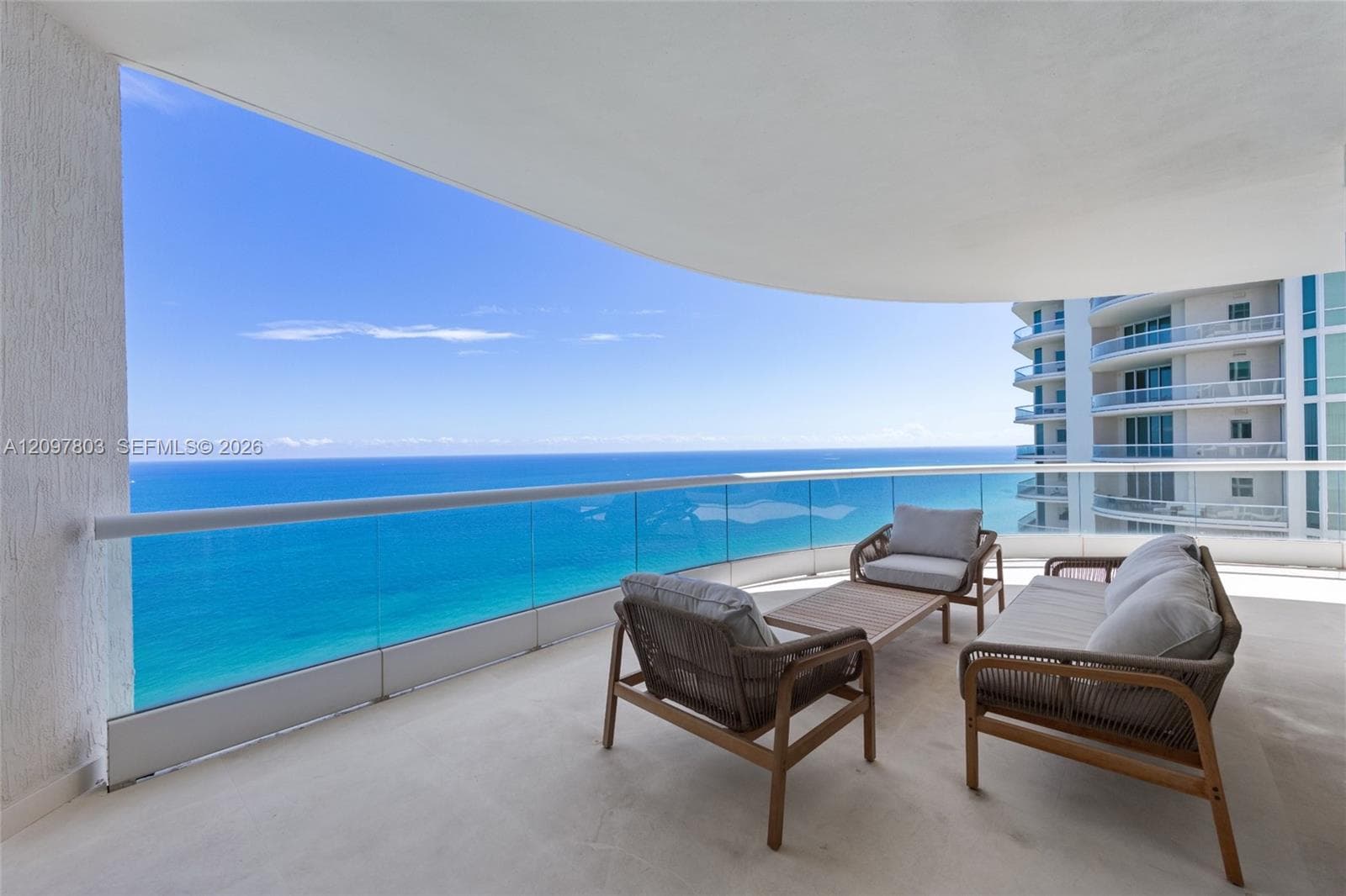 Expansive covered balcony featuring a glass panel railing, concrete flooring, and an unobstructed ocean backdrop