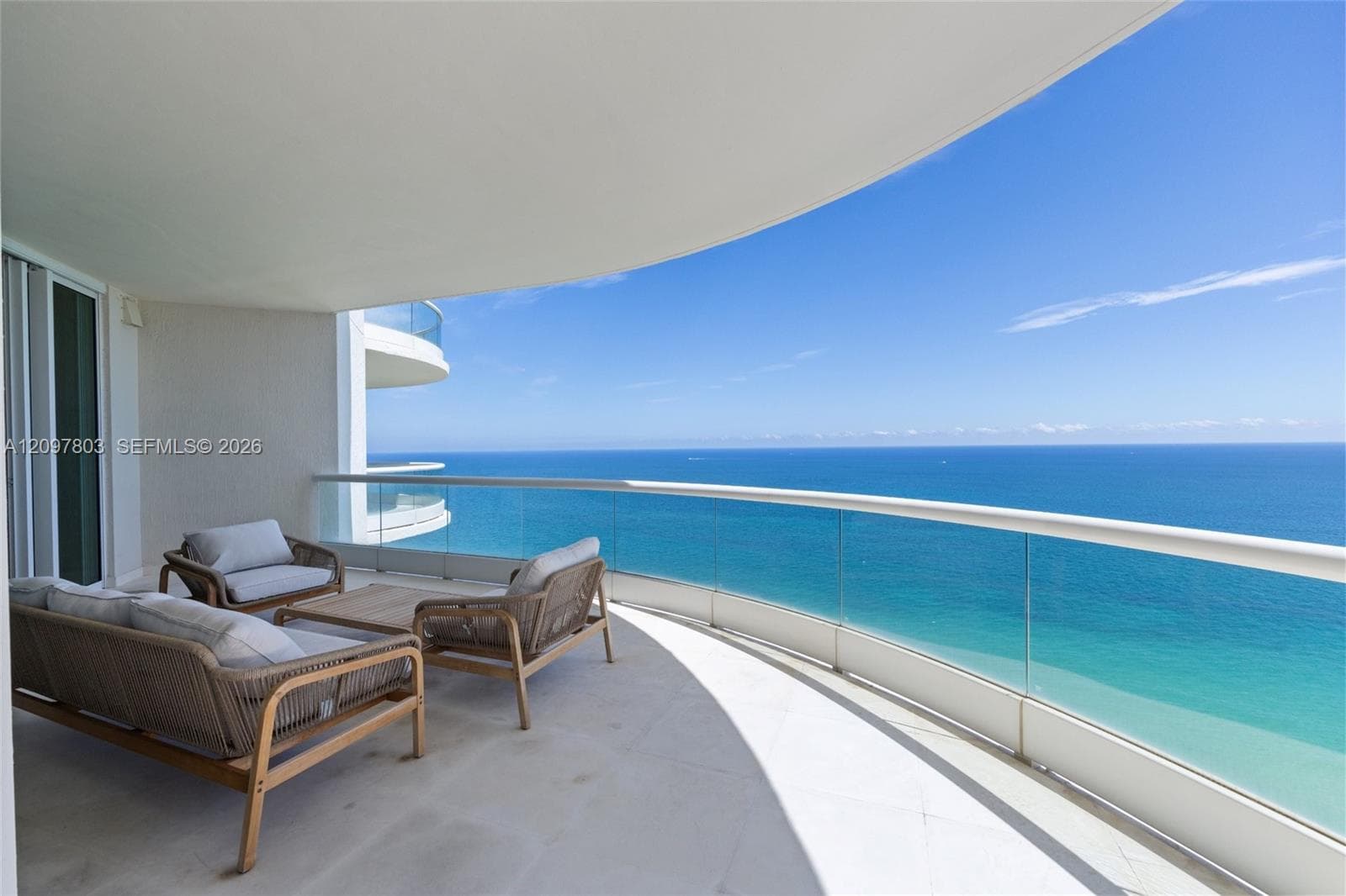 Covered balcony featuring a curved architectural design, concrete flooring, and a glass-paneled railing