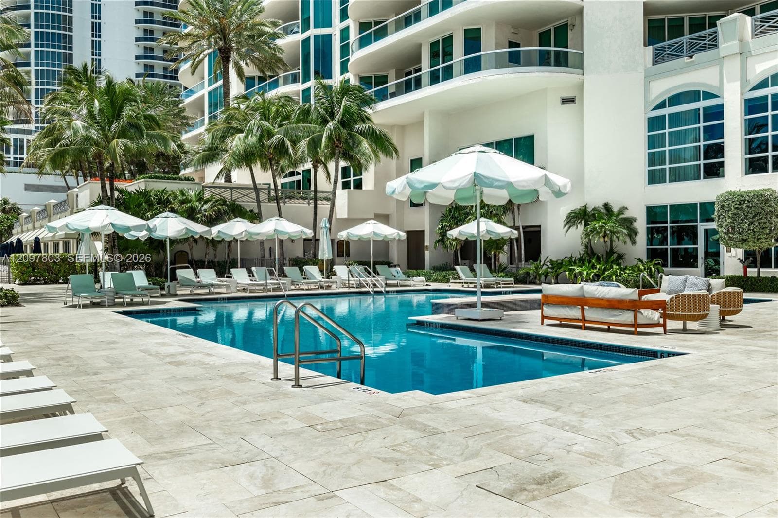 In-ground swimming pool with a stone paver deck, metal pool ladder, and multi-story high-rise architecture featuring balconies