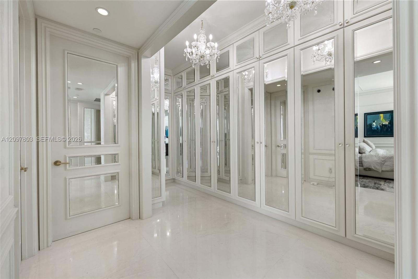 Built-in floor-to-ceiling cabinetry featuring mirrored panel doors, polished stone flooring, custom crystal chandelier lighting, and a paneled door with inset mirror accents