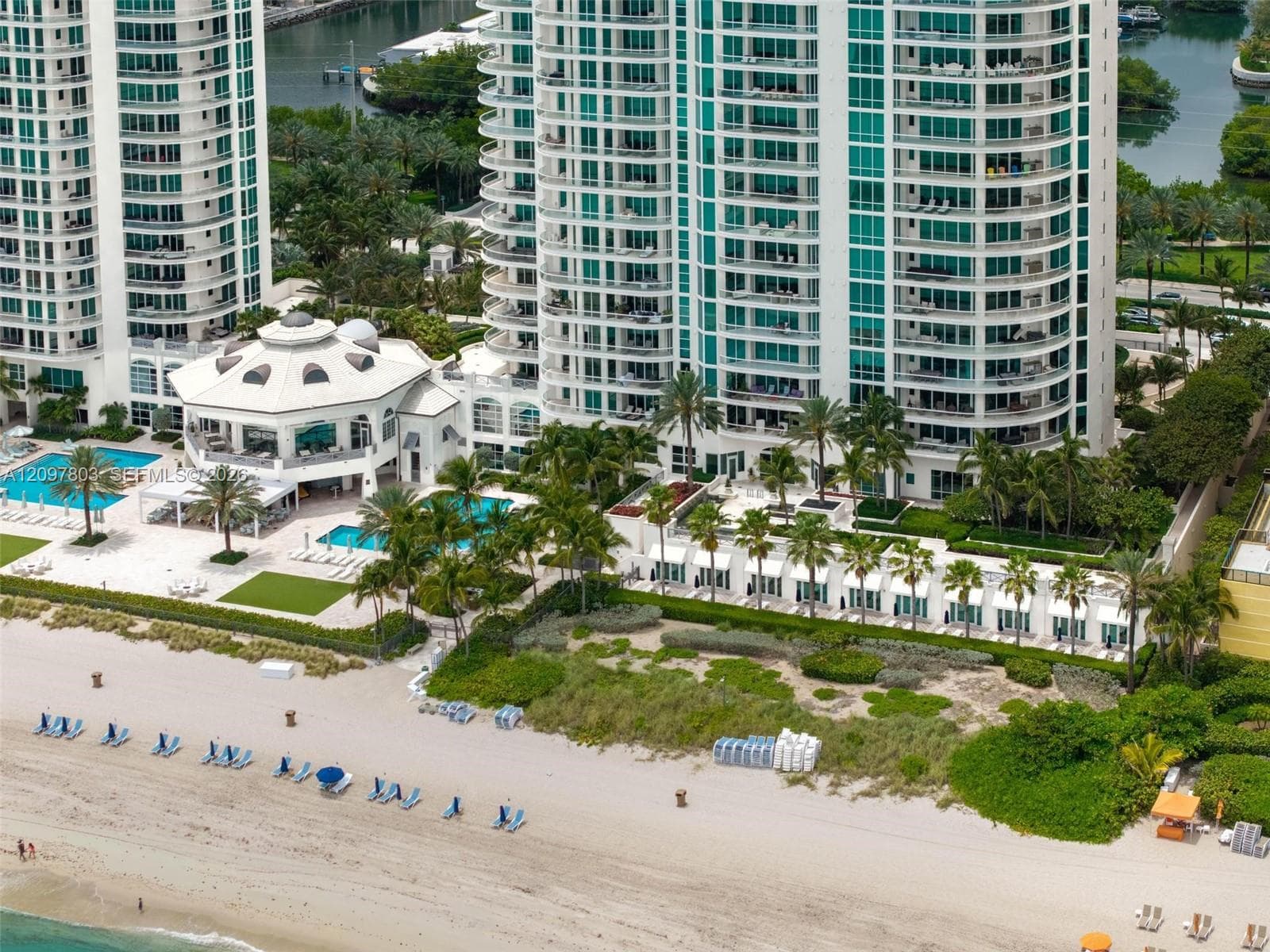 High-rise residential complex featuring private beach access, multiple outdoor swimming pools, manicured tropical landscaping, and a multi-level clubhouse