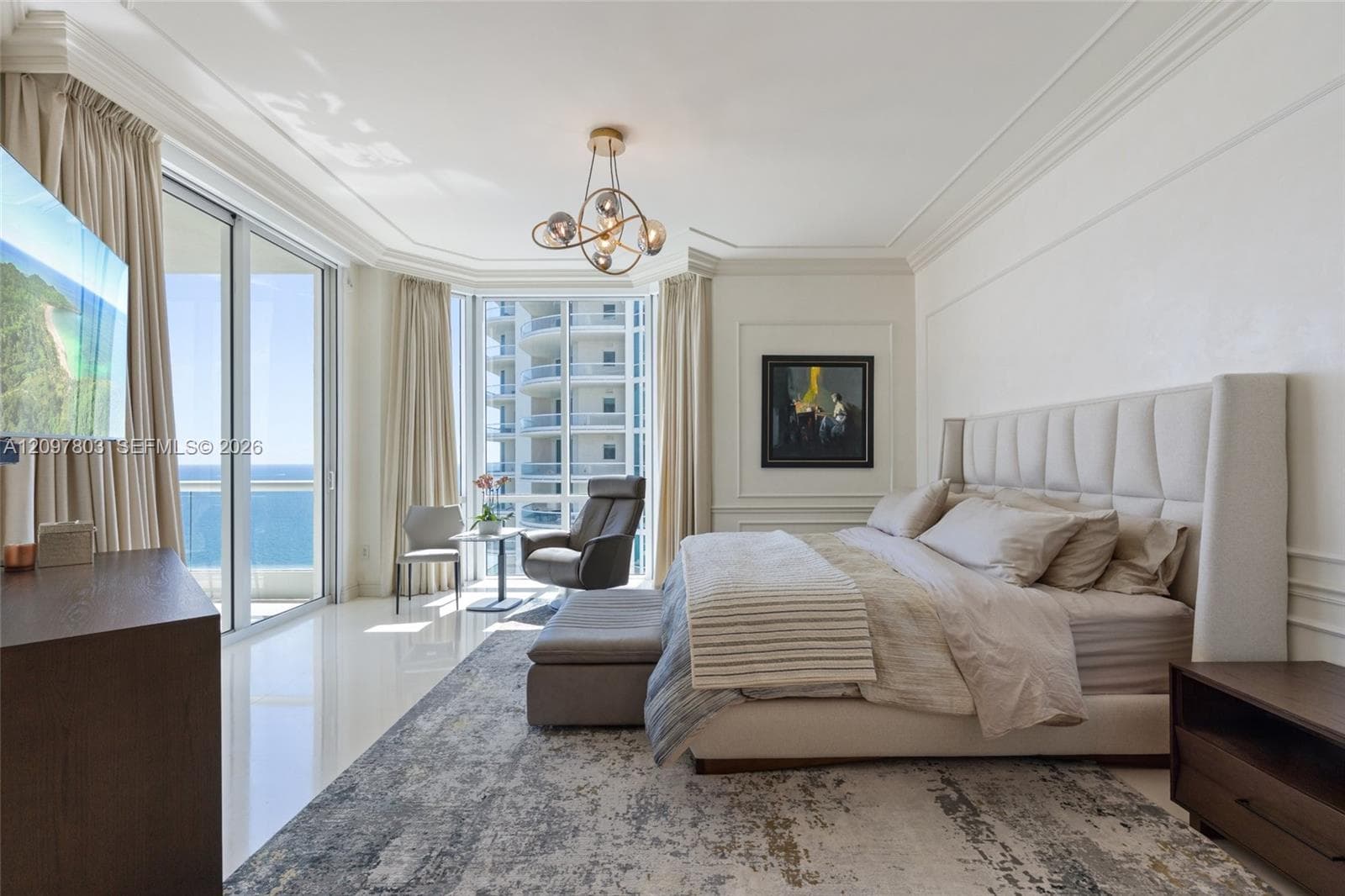 Floor-to-ceiling glass sliding doors, polished tile flooring, tray ceilings with crown molding, custom wall paneling, and a contemporary multi-globe chandelier