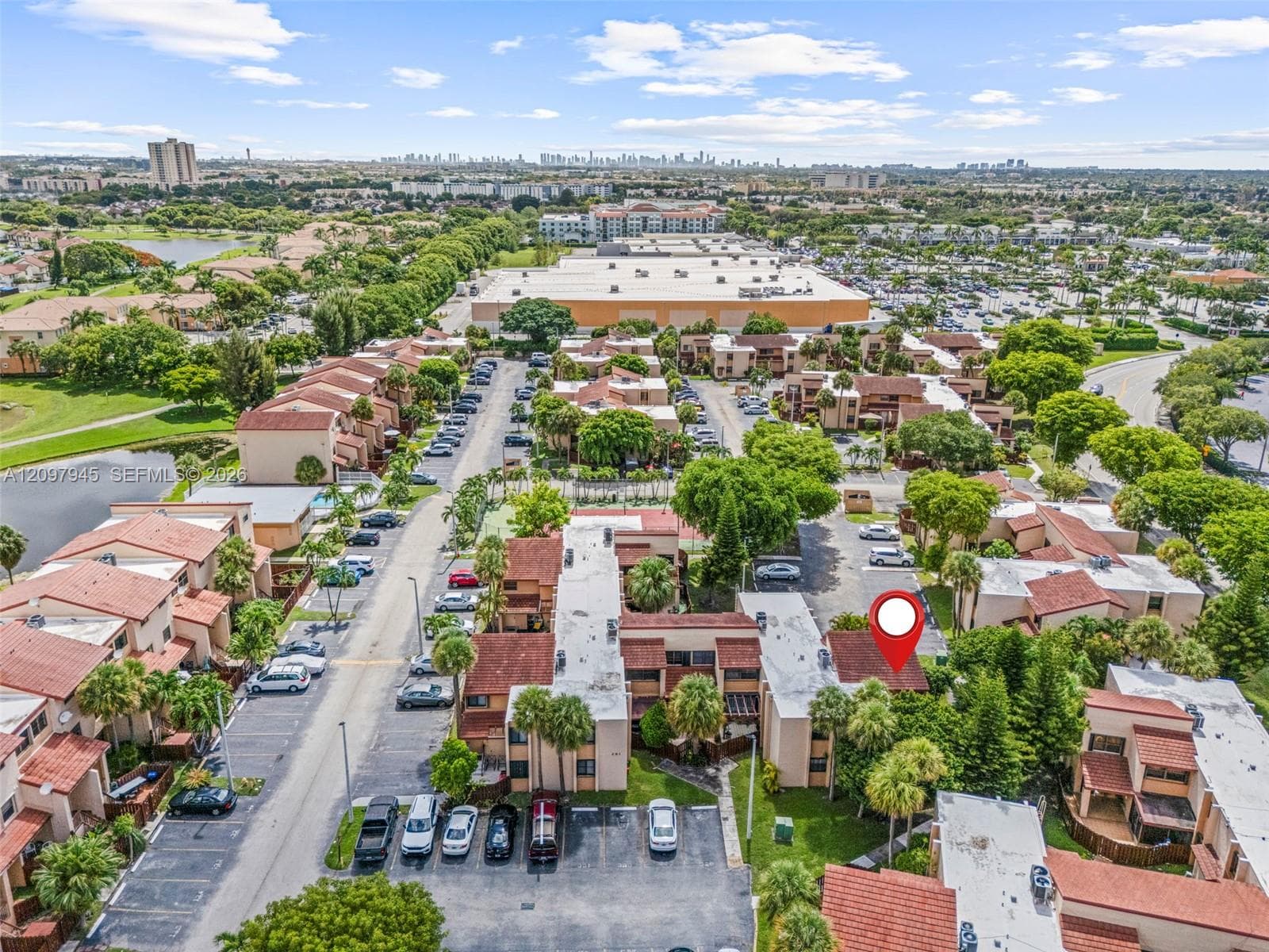 Aerial perspective of a multi-unit residential community featuring clay tile roofing, stucco exterior finishes, designated surface parking, and mature palm landscaping