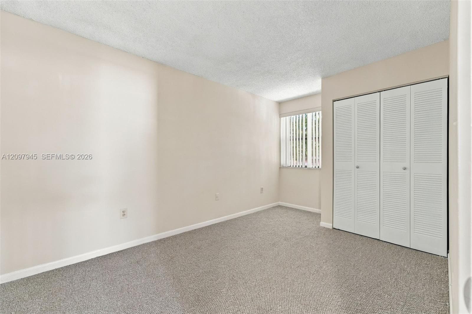 Room featuring neutral-toned walls, carpeting, and a closet with white louvered bi-fold doors