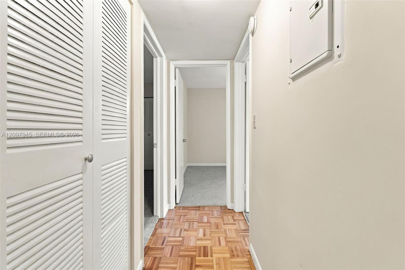 Hallway featuring wood-finish parquet flooring, white louvered closet doors, and neutral wall paint