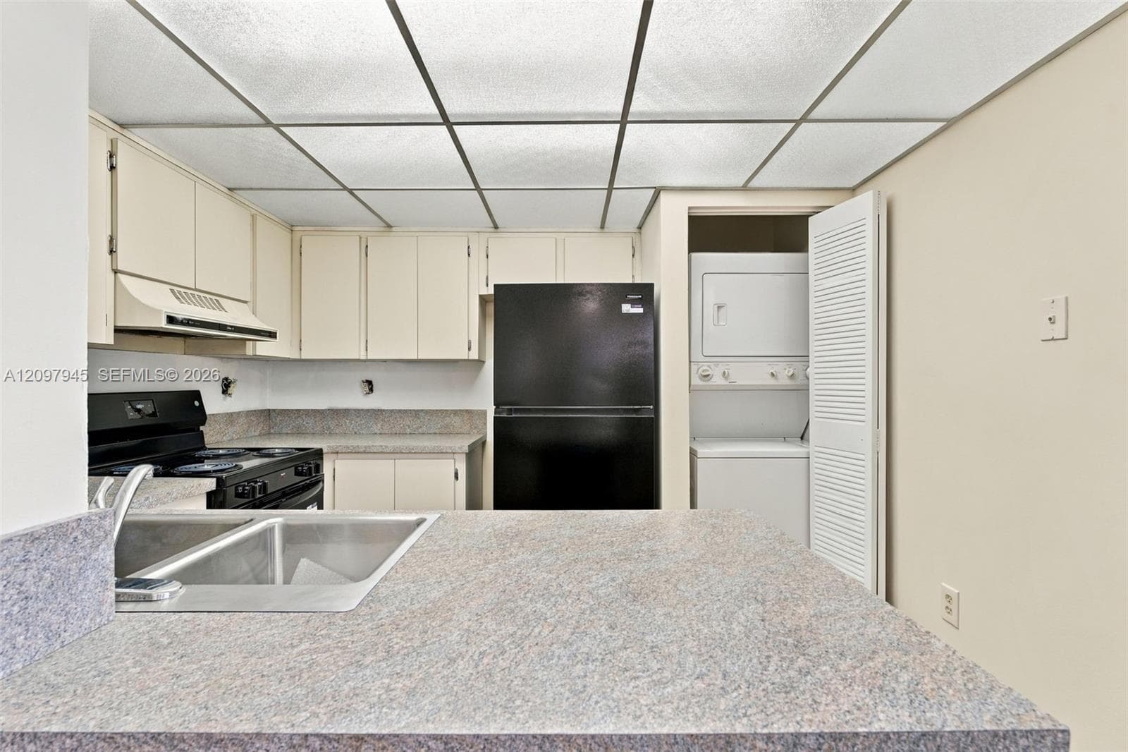 Kitchen featuring cabinetry, stone-finish countertops, dual-basin stainless steel sink, black appliance suite, and a dedicated laundry closet