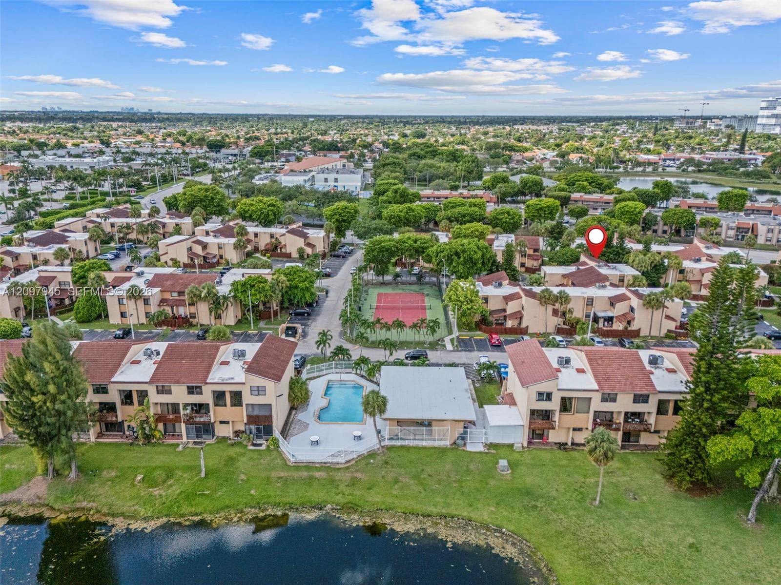 Aerial perspective of a multi-unit residential complex featuring a community swimming pool, tennis court, and waterfront parcel