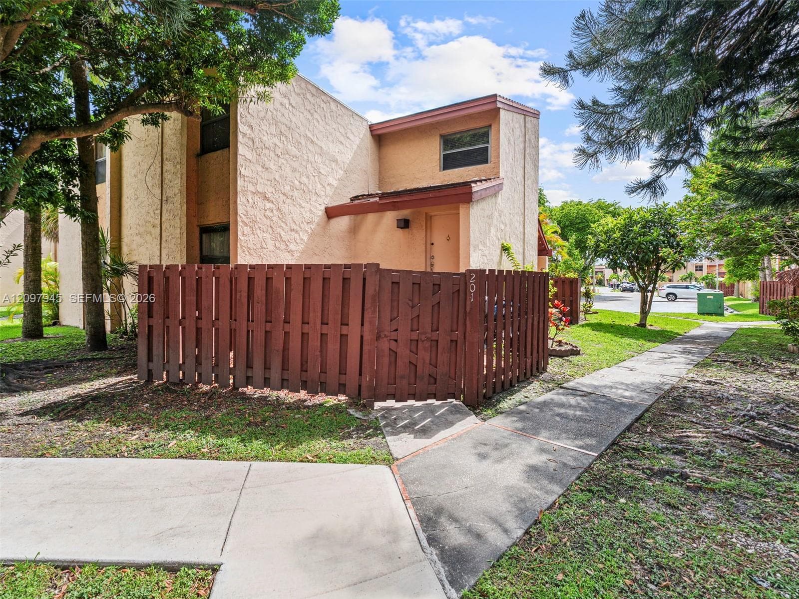 Stucco exterior featuring a private gated courtyard, a pedestrian walkway, and mature landscaping