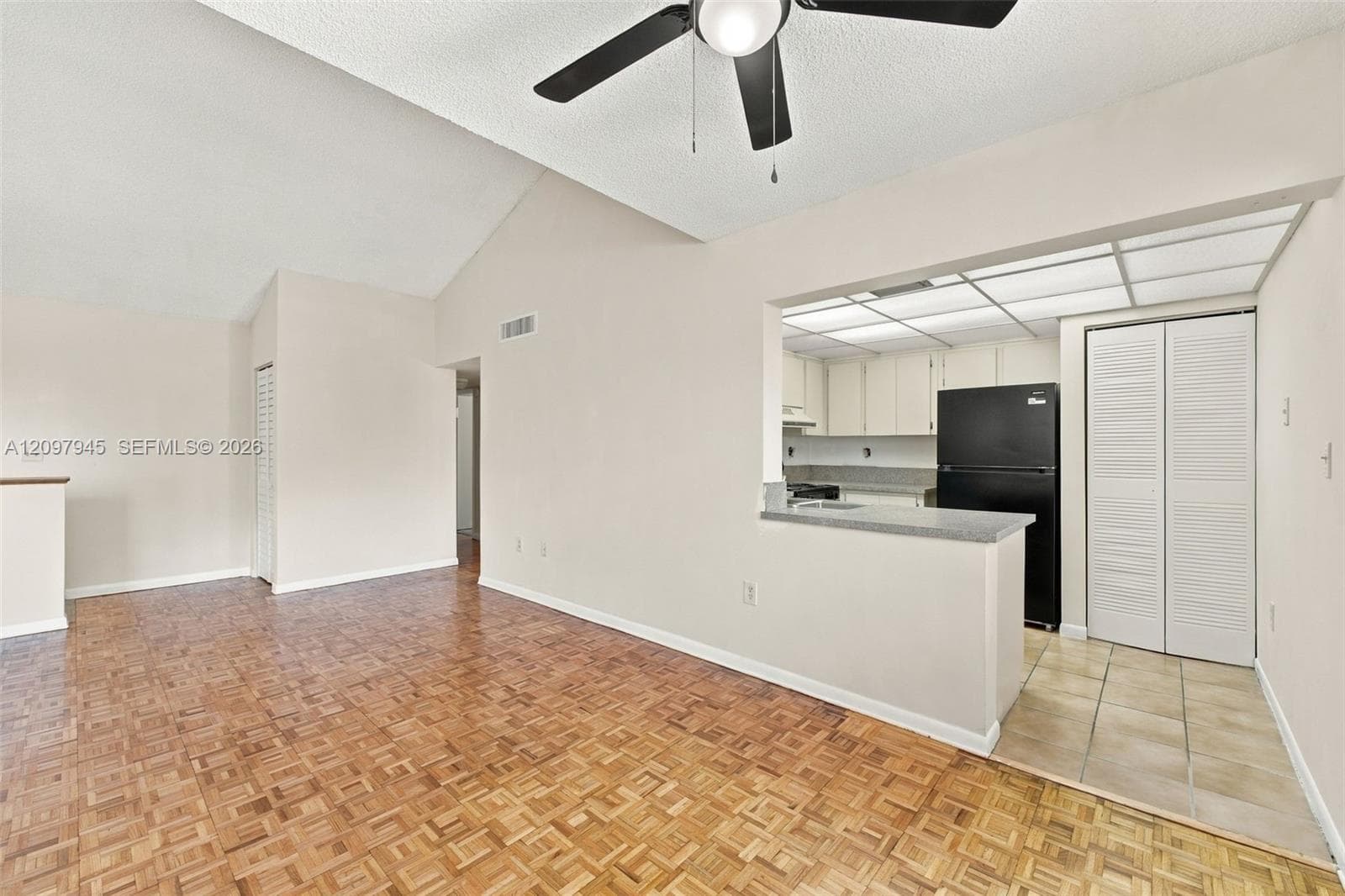 Vaulted ceilings featuring a central overhead fan, parquet wood-finish flooring, breakfast bar with a solid surface countertop, and built-in closet with louvered doors