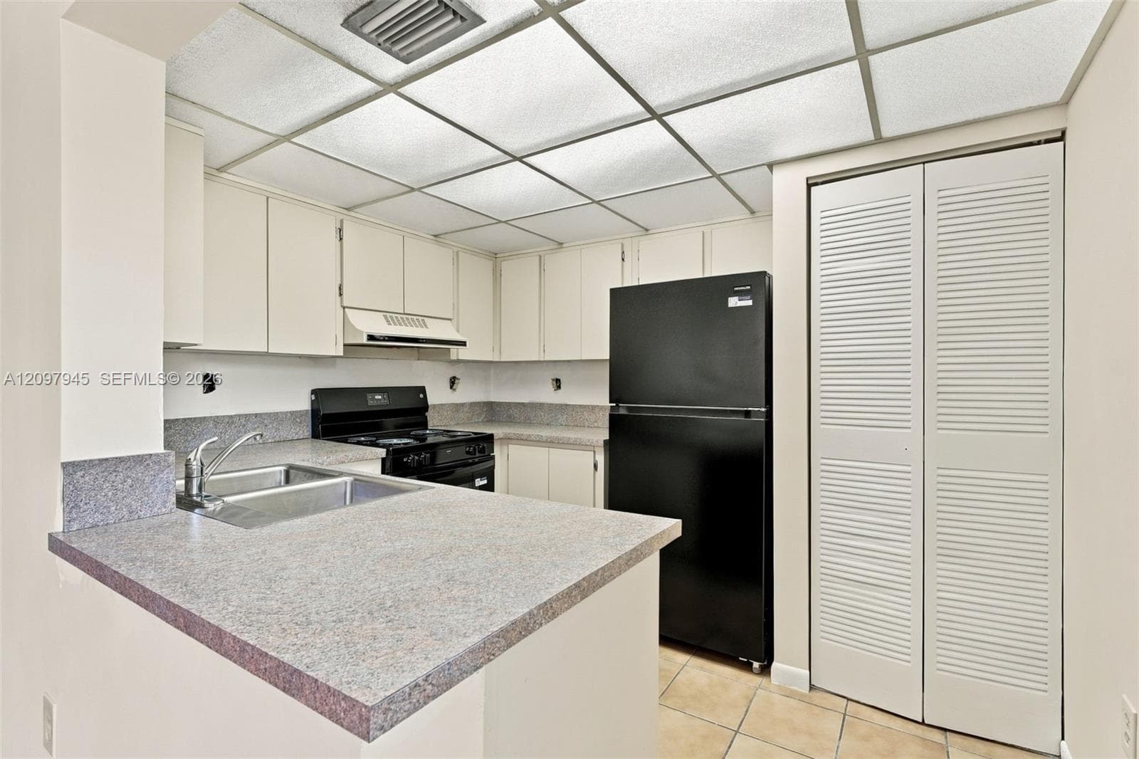 Kitchen featuring flat-panel cabinetry, stone-finish countertops, dual-basin stainless steel sink, tile flooring, and louvered closet doors