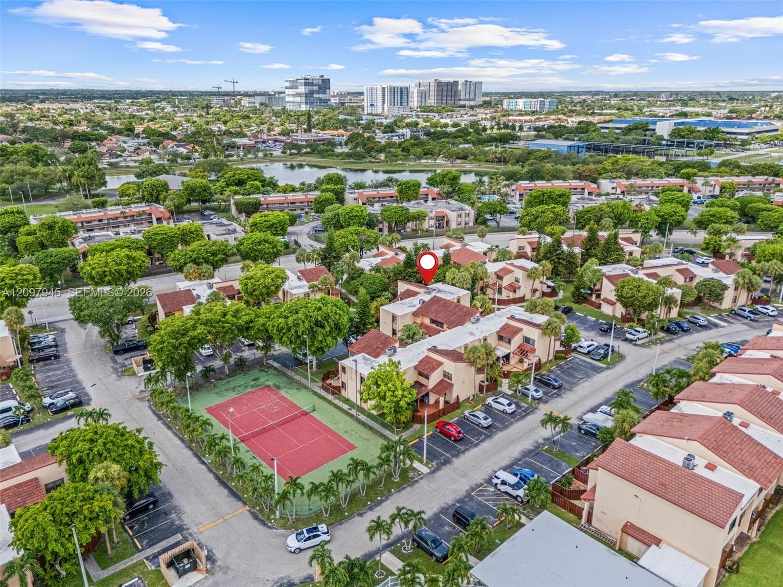 Aerial view of the residential complex featuring a dedicated tennis court, mature landscaping, and multi-level buildings with red tile roofing
