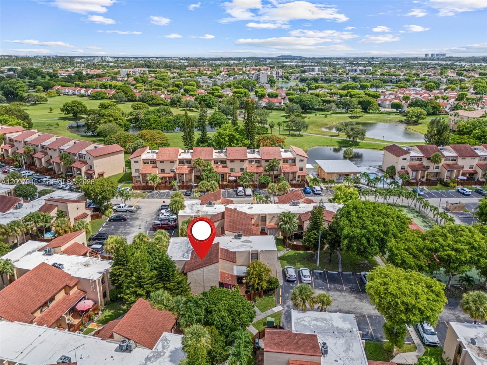 Aerial perspective featuring multi-story residential structures with tile roofing, mature landscaping, and paved parking surfaces
