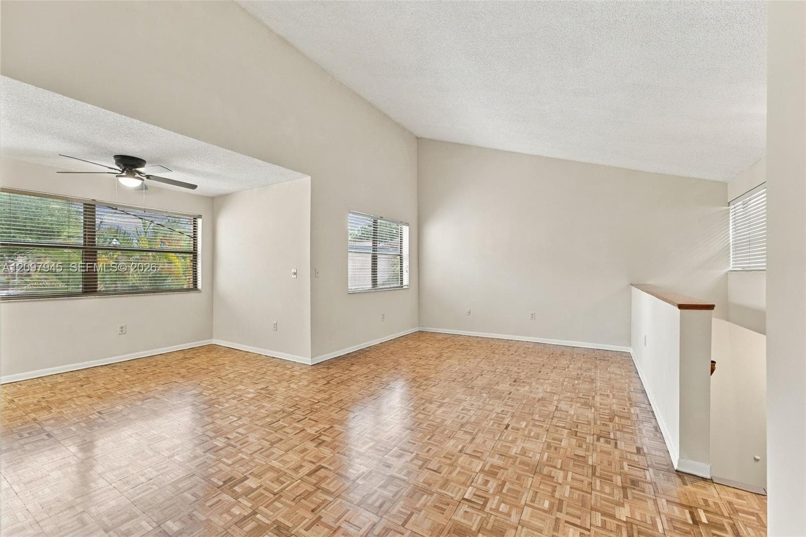 Vaulted ceilings, parquet wood-finish flooring, multi-pane windows, and a ceiling fan with integrated lighting