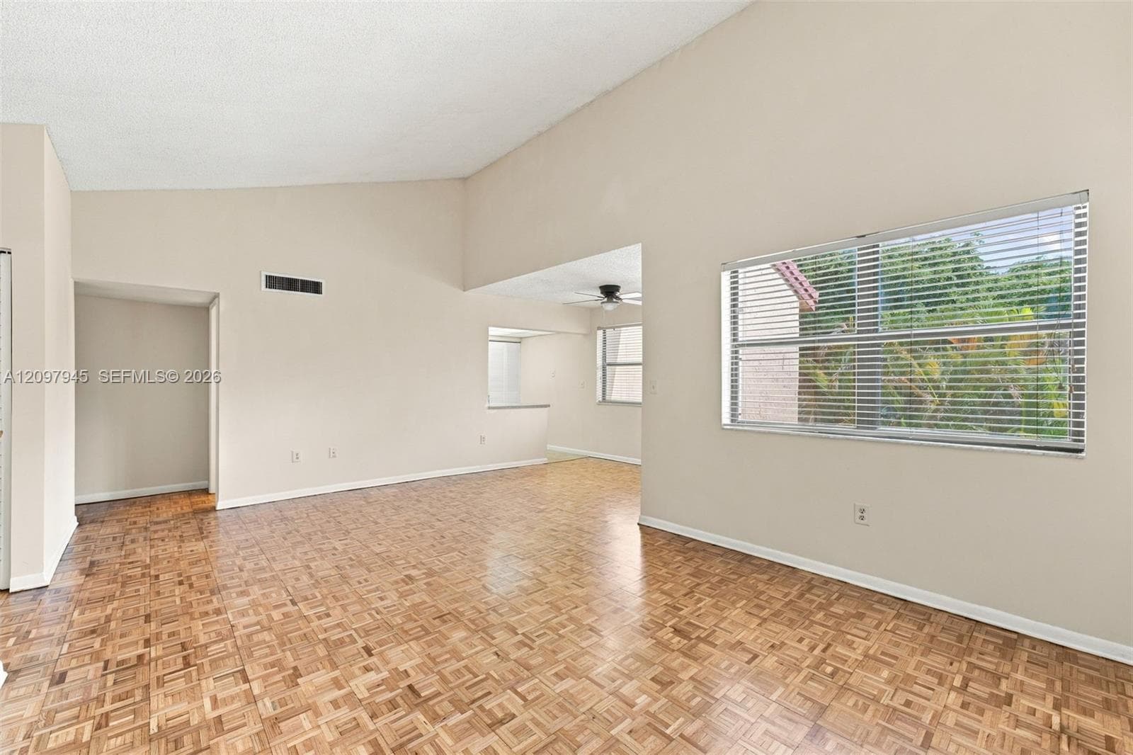 Vaulted ceilings, parquet wood-finish flooring, and large windows with horizontal blinds